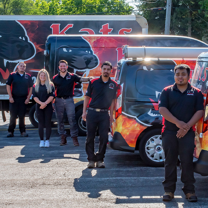 Heating technicians standing beside their Kats Heating & Cooling service vehicles