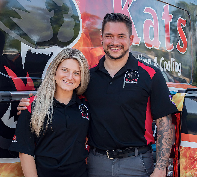 The owner of the company, Giovanni Katsigiannis, and his wife standing next to a company service truck. Both are wearing black polo shirts with the company logo on them.