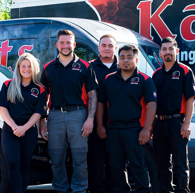 Heating technicians standing beside their Kats Heating & Cooling service vehicles
