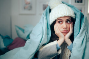 A young woman wrapped in a blanket and wearing a stocking cap, miserable in her unheated home.